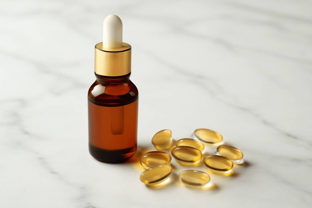 Butelka oleju odżywczego i kapsułki z witaminą E na marmurowej powierzchni.