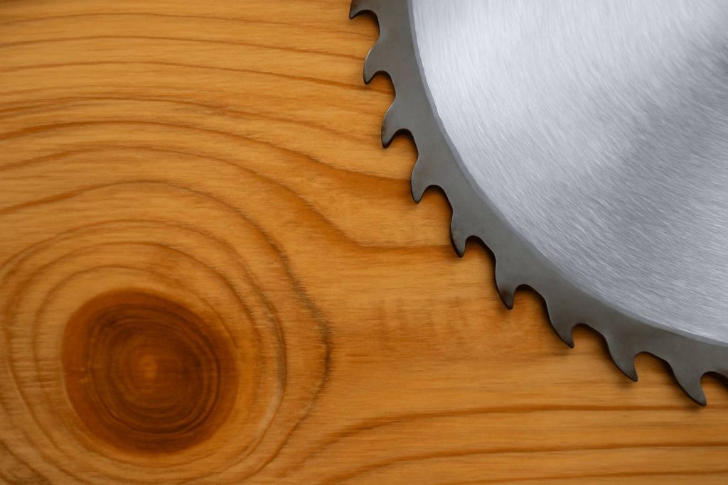 Zbliżenie na teksturę drewna sosny, z widoczną piłą – ukazuje proces przygotowania drewna do budowy mebli.